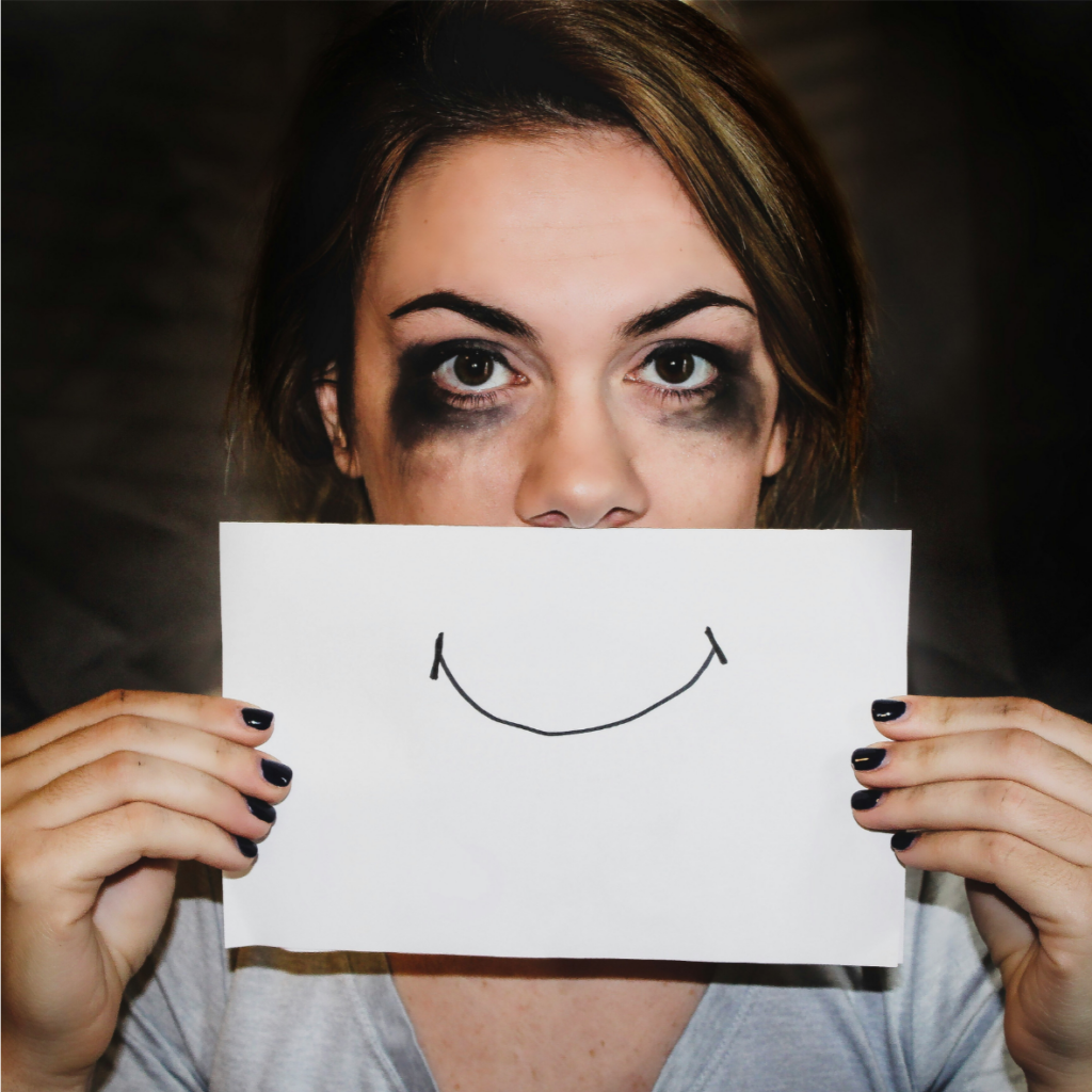 Une femme tenant un papier avec un visage souriant, faisant la promotion de la santé mentale.