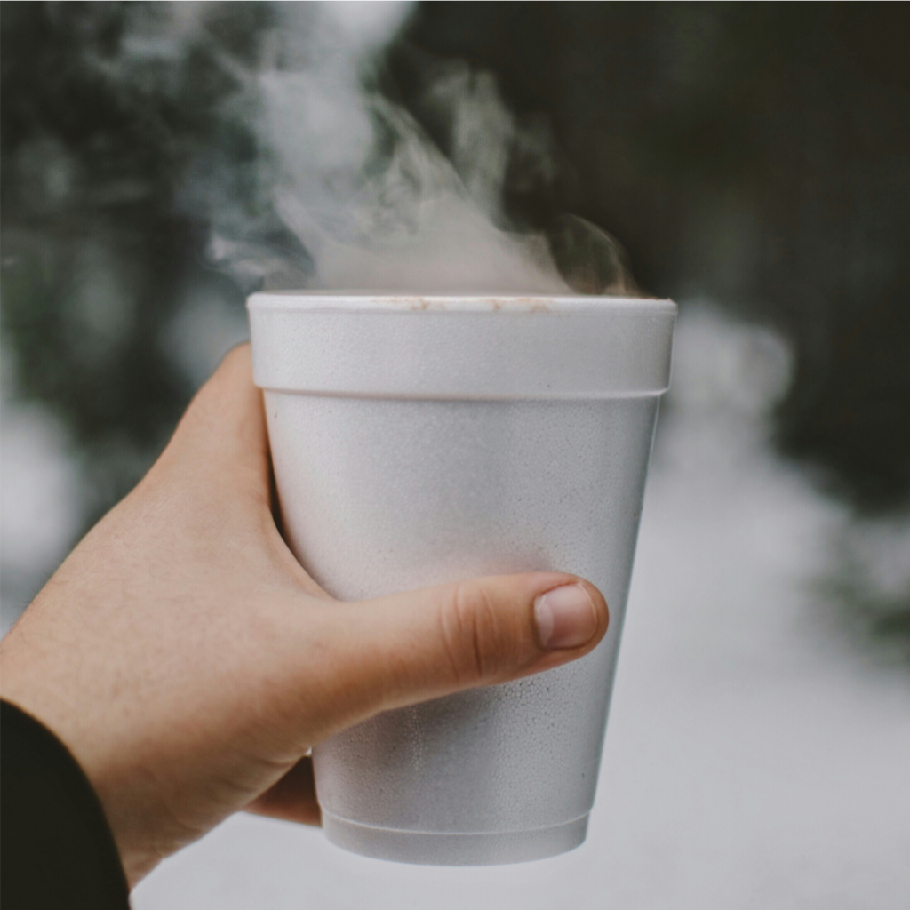 Une main tenant une tasse fumante sur un fond enneigé.